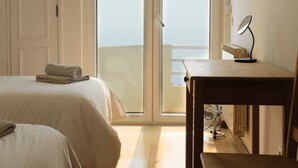 Une chambre avec deux lits, un bureau et une chaise. Une porte-fenêtre coulissante donne sur un balcon.