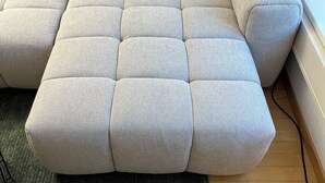 A sectional sofa with a light fabric, positioned on a dark green rug, against a wooden floor and a white wall. - ODA Suites (Lucerne)
