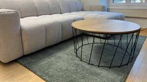 A light-colored sofa with a round wooden table in front of it, placed on a green rug. - ODA Suites (Lucerne)