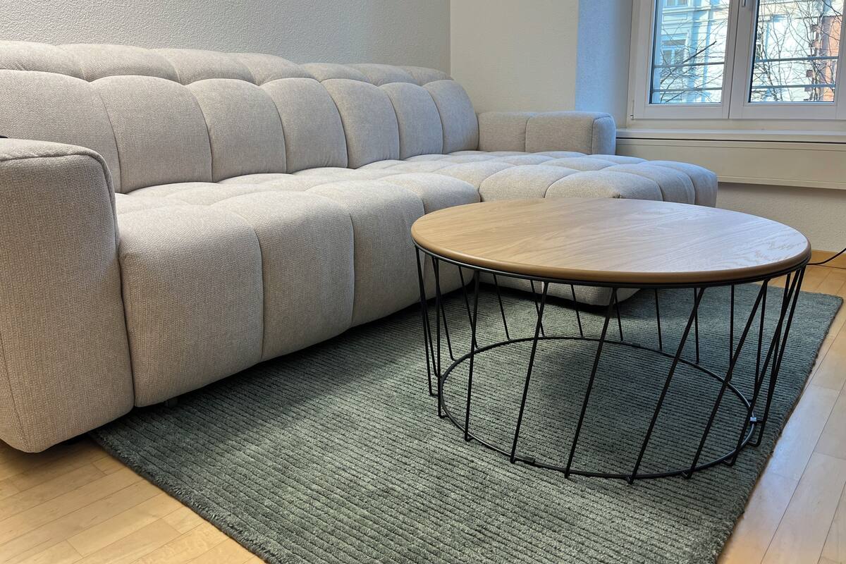 A light-colored sofa with a round wooden table in front of it, placed on a green rug.