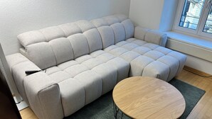 A modern living room with a grey sofa, a round wooden coffee table, and a view of the outside through a window. - ODA Suites (Lucerne)