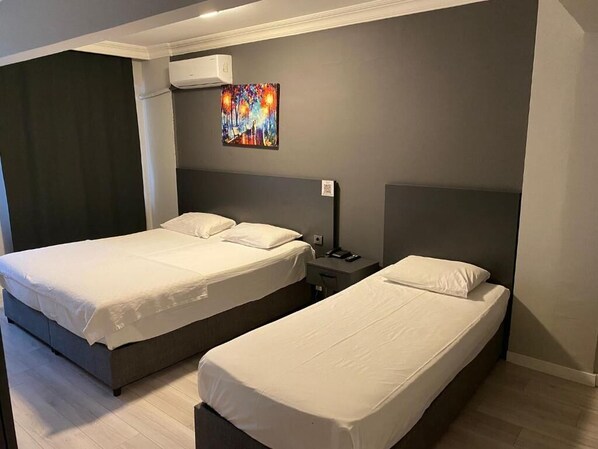 A hotel room with two beds, a painting on the wall, and a nightstand with a lamp. - ATABAY OTEL (İstanbul)