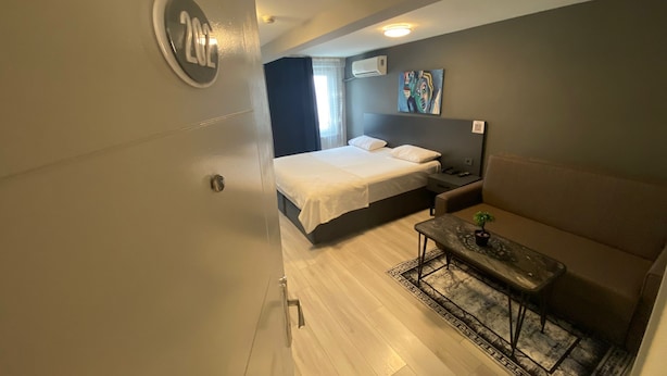 Ein kleines Hotelzimmer mit Bett, einer kleinen Sitzecke, einem Nachttisch und einer Wandklimaanlage.