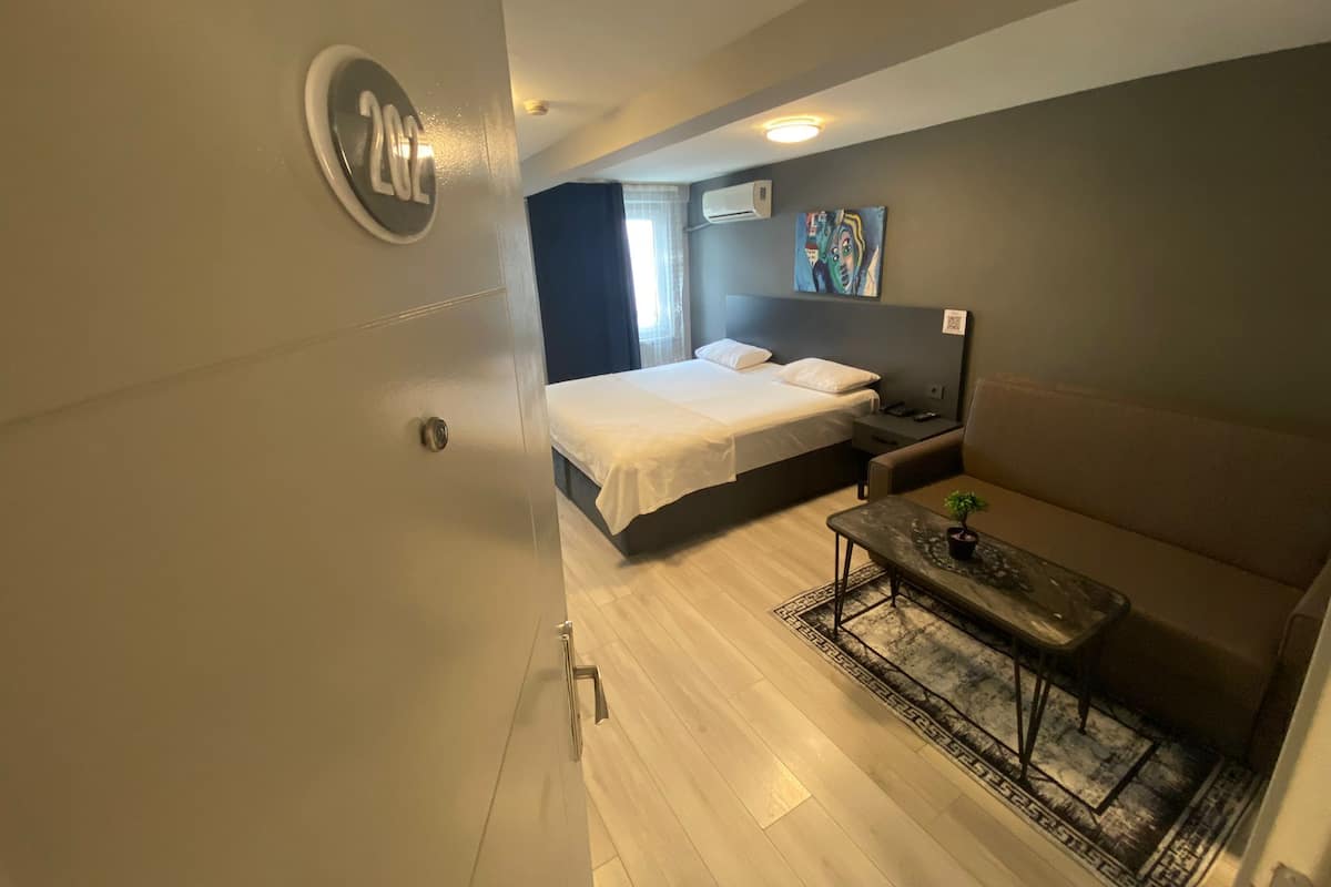 Habitación de hotel pequeña con cama, un sofá compacto, una mesita de noche y aire acondicionado instalado en la pared.