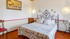 A bedroom with a wooden ceiling, a bed with a floral bedspread, a nightstand, a chair, and a wall-mounted lamp. - Former convent with private pool in Tuscany (Camaiore)