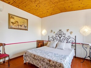 A bedroom with a wooden ceiling, a bed with a floral bedspread, a nightstand, a chair, and a wall-mounted lamp. - Former convent with private pool in Tuscany (Camaiore)