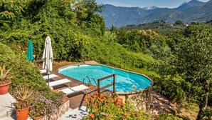 A swimming pool with a wooden deck, surrounded by lush greenery and mountains in the background. - Former convent with private pool in Tuscany (Camaiore)