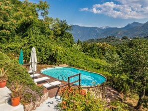 A swimming pool with a wooden deck, surrounded by lush greenery and mountains in the background. - Former convent with private pool in Tuscany (Camaiore)