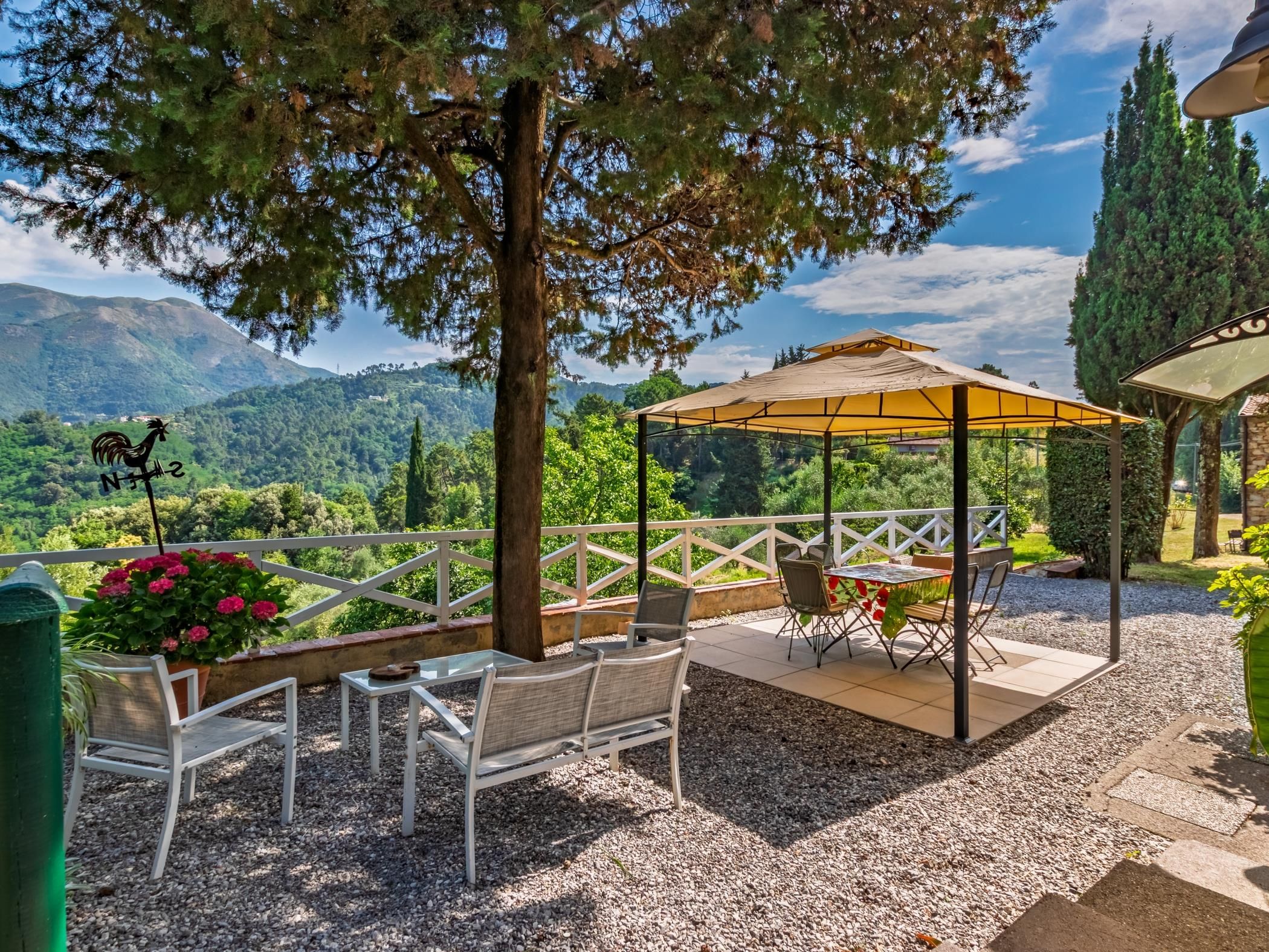 Een terras met een pergola, stoelen en een tafel, met uitzicht op een bergachtig landschap.