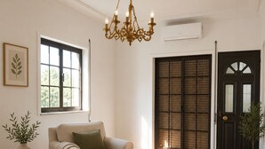 A living room with a beige sofa, a round coffee table, a chandelier, a potted plant, and a large window. - 1-Bedroom Apartment in Amares, Braga (September through June) (Barreiros)