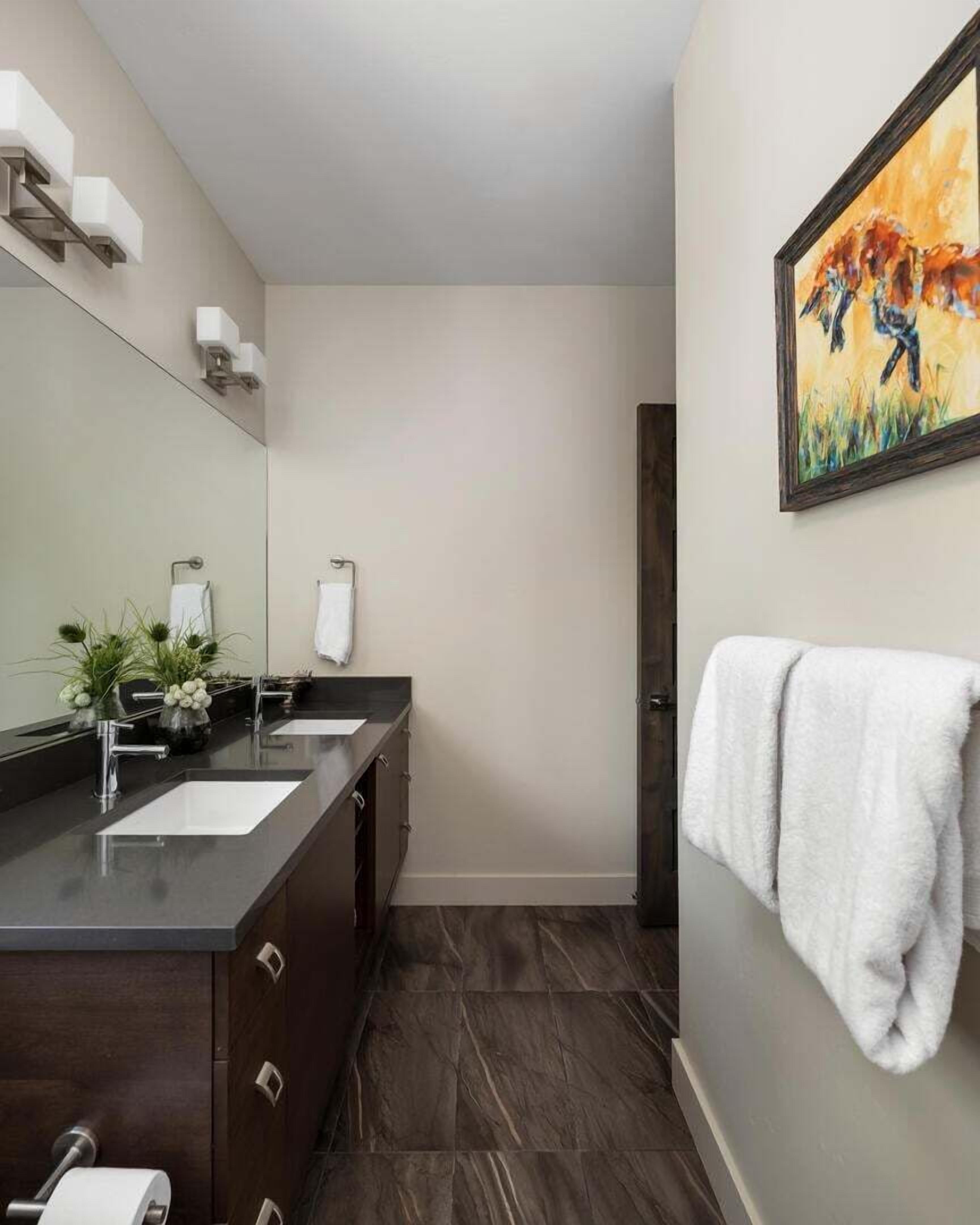 Une salle de bain moderne avec un meuble-lavabo en bois foncé, deux vasques, un grand miroir et un tableau accroché au mur.