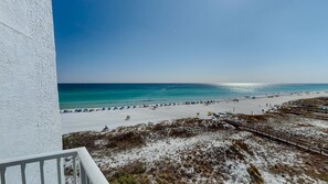 A beach view with a white building, sandy beach, and clear blue water. - Mainsail 152 2 Bedroom Condo (Miramar Beach)