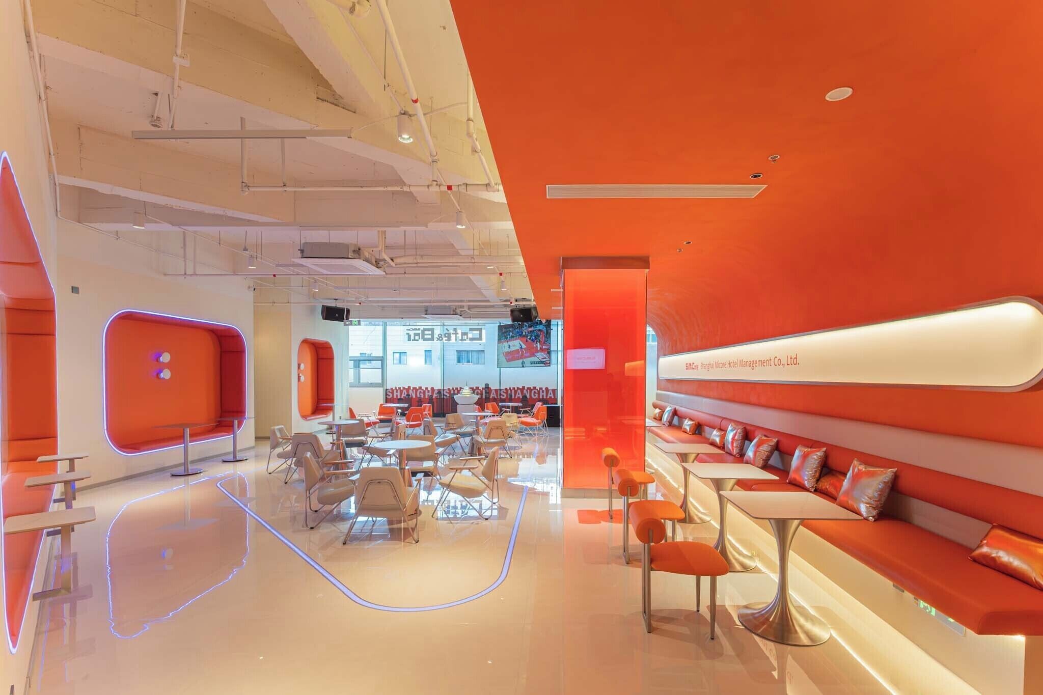 Eine moderne Hotellobby mit einem leuchtend orangefarbenen Design, Sitzbereichen und einem sichtbaren Schild des Hotelmanagementunternehmens.