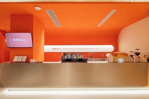 A hotel reception area with a modern design, featuring a prominent orange color scheme, a digital screen displaying 'SIM:Core', and a bar area with various bottles and glasses. - SilMiCore Hostel (Shanghai)