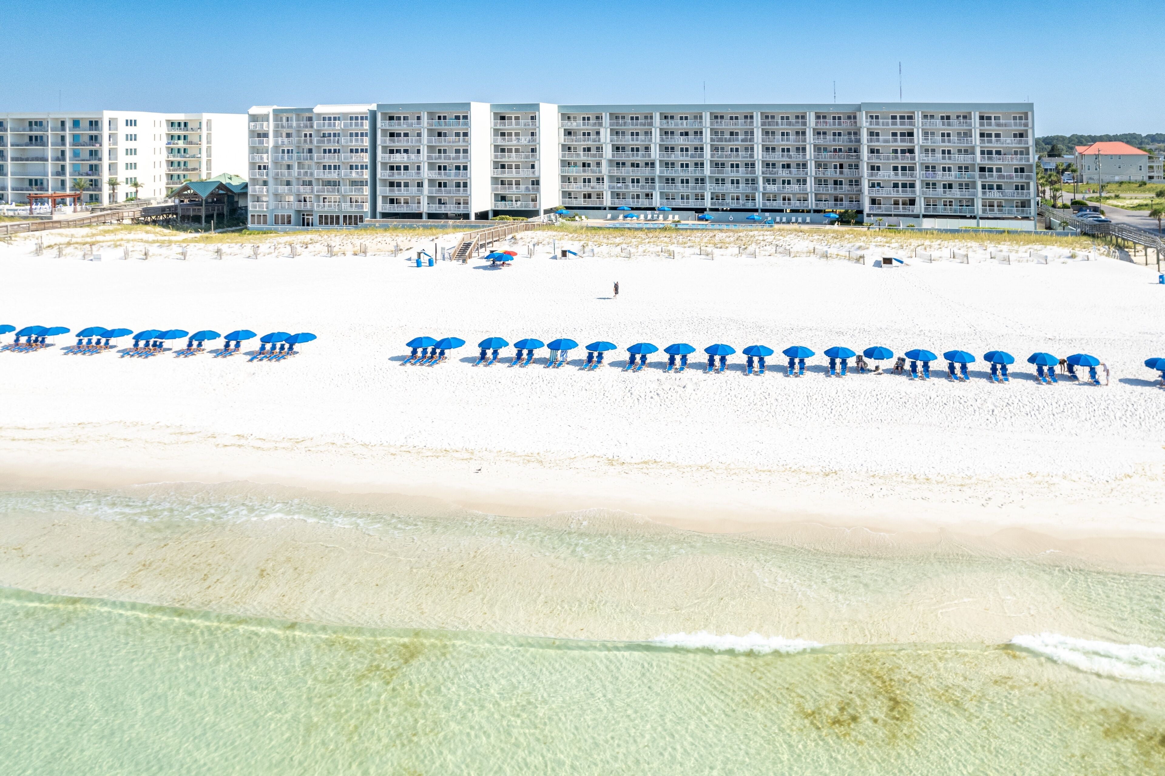 A beachfront hotel with multiple balconies, a sandy beach, and umbrellas.