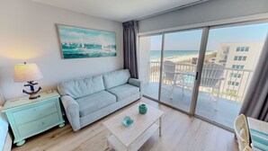 A room with a sofa, a table, a lamp, a painting, and a balcony with a view of the beach. - Islander Beach Resort 705 Condo (Fort Walton Beach)