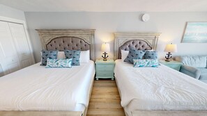 Een hotelkamer met twee bedden, een nachtkastje met lampen en een schilderij aan de muur.
