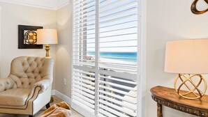 Une chambre avec vue sur la plage, un fauteuil à capitons, une lampe et une petite table en bois.