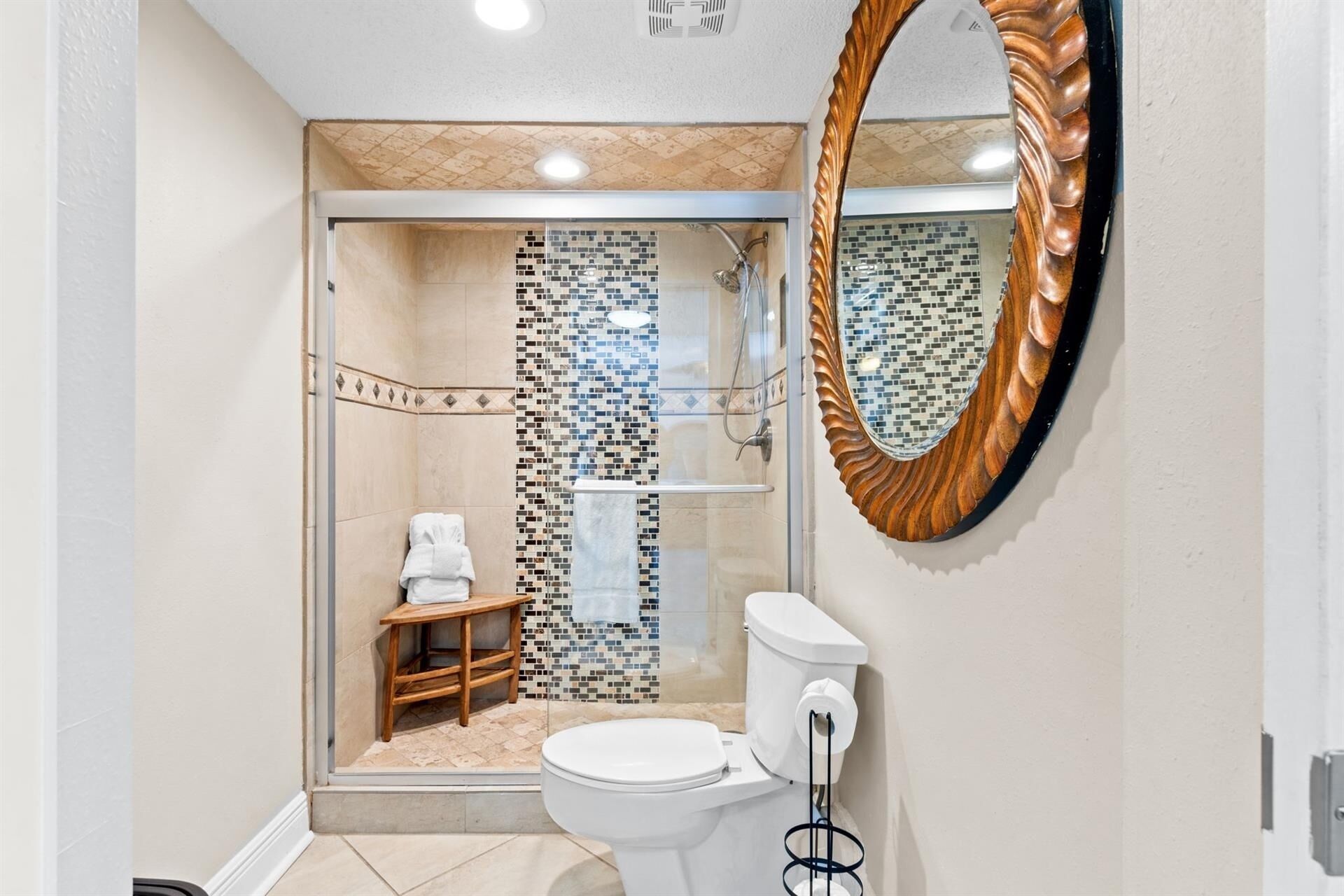 Une salle de bain moderne avec une douche à parois de verre, des toilettes et un tabouret en bois.