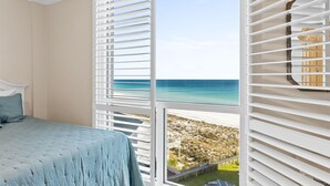 Une chambre avec un lit, une vue sur la plage et un balcon avec des stores blancs.