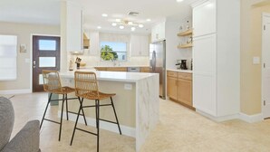 A modern kitchen with white cabinetry, a marble island, and two wicker bar stools. - Nst108 4 Bedroom Home (Punta Gorda)