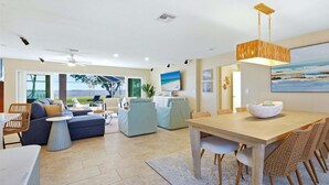 A spacious living area with a large window overlooking a scenic view, a dining area with a wooden table and wicker chairs, and a cozy seating area with sofas and a coffee table. - Nst108 4 Bedroom Home (Punta Gorda)
