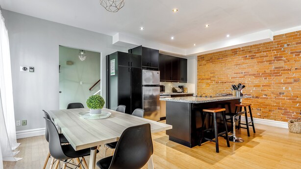 Une cuisine moderne avec un mur en briques, un coin repas avec une table et des chaises en bois, et un petit îlot avec des tabourets.