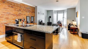 Une cuisine moderne dotée d’un plan de travail en granit, d’un four encastré et d’un mur en briques.