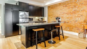 Une cuisine moderne avec des meubles de couleur sombre, un plan de travail en granit et un mur en briques.
