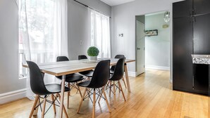 Un espace repas moderne avec une table en bois et des chaises noires, une plante en pot, et une cuisine dotée d’un meuble noir et d’un plan de travail en marbre.