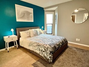 A bedroom with a bed, nightstands, a large window, and a mirror on the wall. - Gulfside Townhome 3 2 Bedroom Townhouse (Gulf Shores)