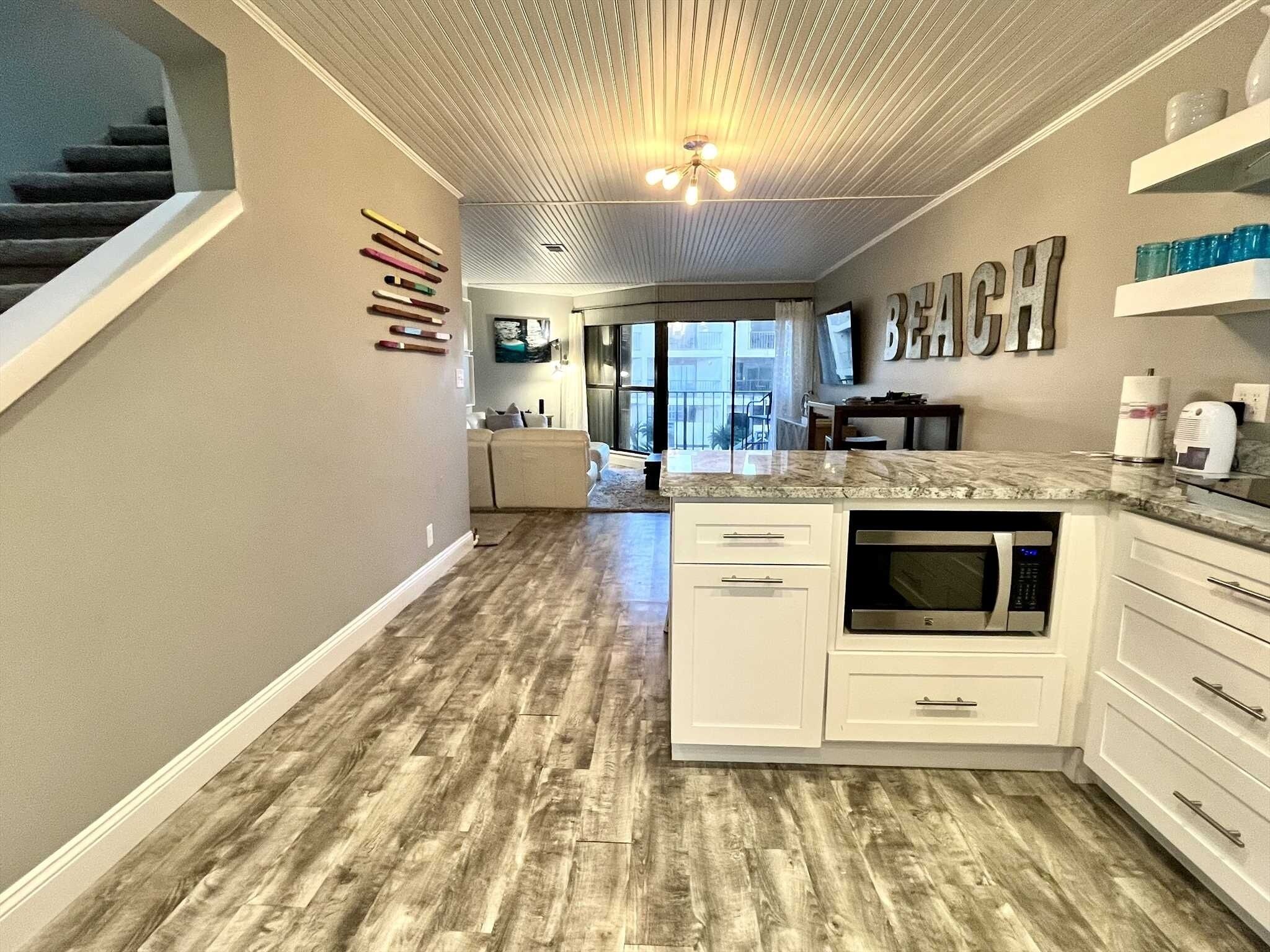 A modern kitchen with white cabinets, a built-in microwave, and a wooden floor.