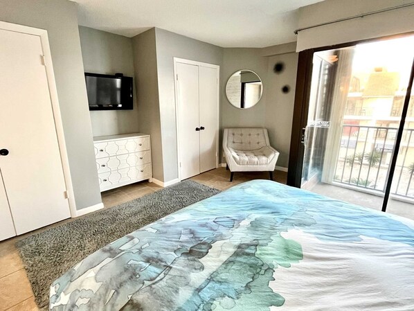 Un dormitorio con cama, cómoda, silla, televisor y balcón.