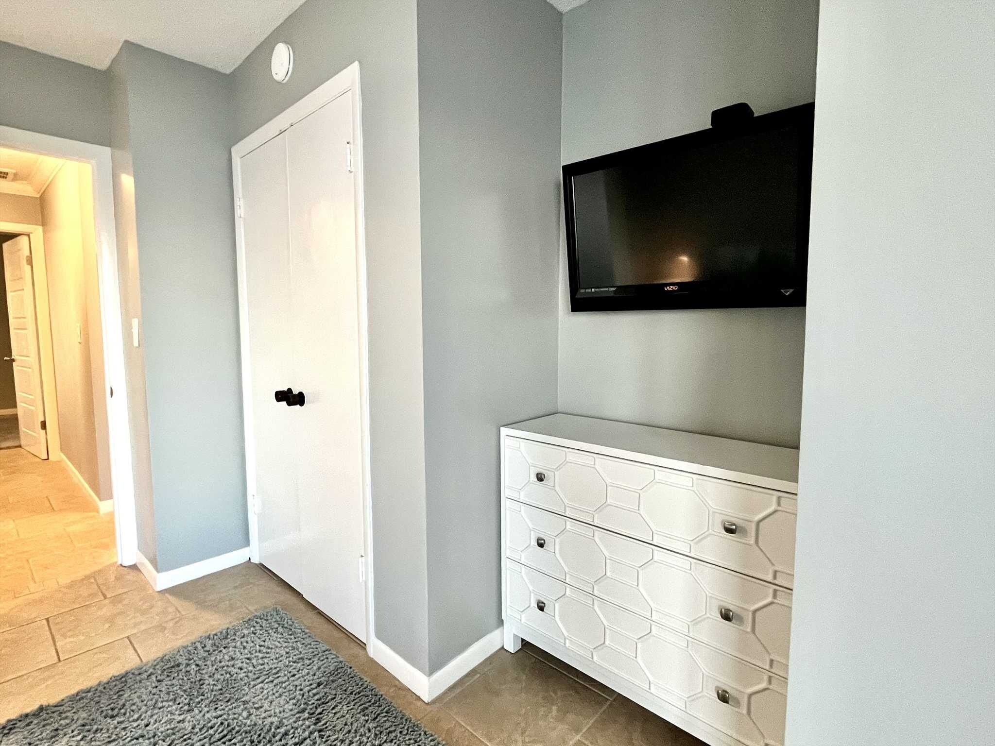 Una habitación con una puerta blanca, un aparador blanco con diseños hexagonales y un televisor montado en la pared.