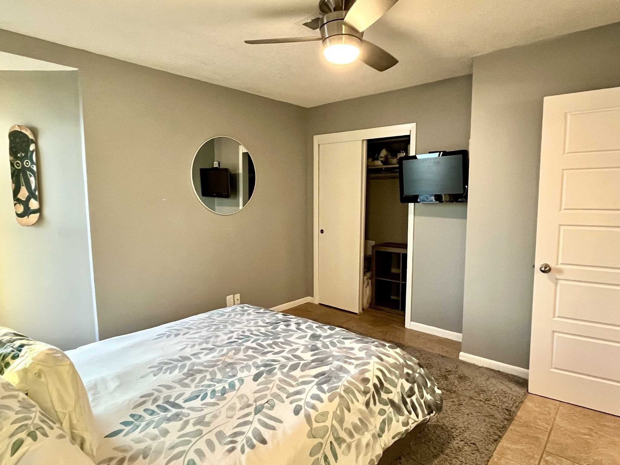 Une chambre à coucher comprenant un lit, un ventilateur de plafond, un miroir, une télévision et un placard.