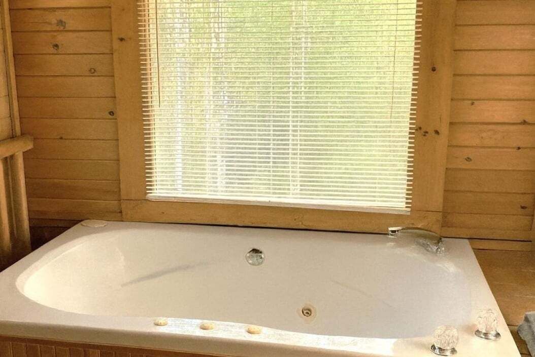 Una cabaña de madera con una bañera grande, una ventana con persianas y una puerta de madera.
