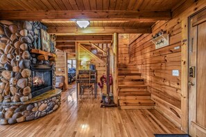 A wooden interior with a stone fireplace, wooden walls, and a staircase leading to another level. - Rise And Shine 3 Bedroom Cabin (Gatlinburg)