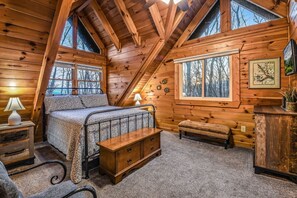 A cozy cabin bedroom with a bed, bench, dresser, and a window with a view of trees. - Rise And Shine 3 Bedroom Cabin (Gatlinburg)