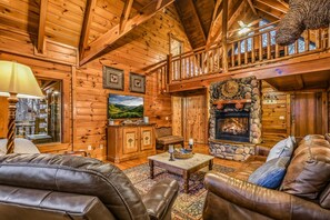 A log cabin interior with a fireplace, leather furniture, and framed pictures on the walls. - Rise And Shine 3 Bedroom Cabin (Gatlinburg)