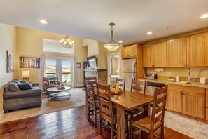 A modern kitchen with wooden cabinets, a dining table with chairs, a sofa, and a coffee table. - Base Camp 402 2 Bedroom Condo (Granby)