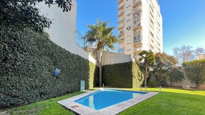 Une piscine rectangulaire entourée d’une pelouse bien entretenue et d’une haie imposante.