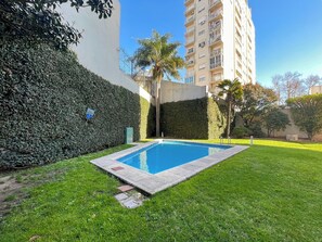 Una piscina rectangular rodeada por un césped cuidado y un seto alto.
