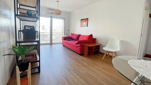 Un salon moderne avec un canapé rouge, un fauteuil blanc, une table basse en verre et un plancher en bois.