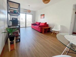 Una sala de estar moderna con un sofá rojo, una silla blanca, una mesa de centro de vidrio y suelo de madera.