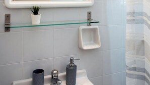 Ein Badezimmer mit einem weißen Waschbecken, einer Glasablage mit einem Topfpflanzen, einer kleinen Seifenschale und einer Duschvorhang.
