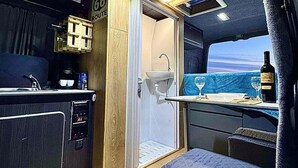 A compact kitchen with a sink, coffee machine, and a small dining area with a table and chairs. - Campervan Tirana Leoventure (Tirana)