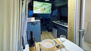 A compact kitchen with a dining area set for two, featuring a television, a wine bottle, and a meal set. - Campervan Tirana Leoventure (Tirana)