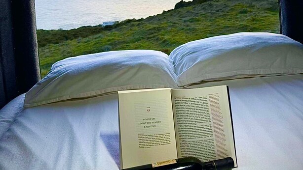 A bed with an open book and a pen, set against a view of the sea and a sunset. - Campervan Tirana Leoventure (Tirana)