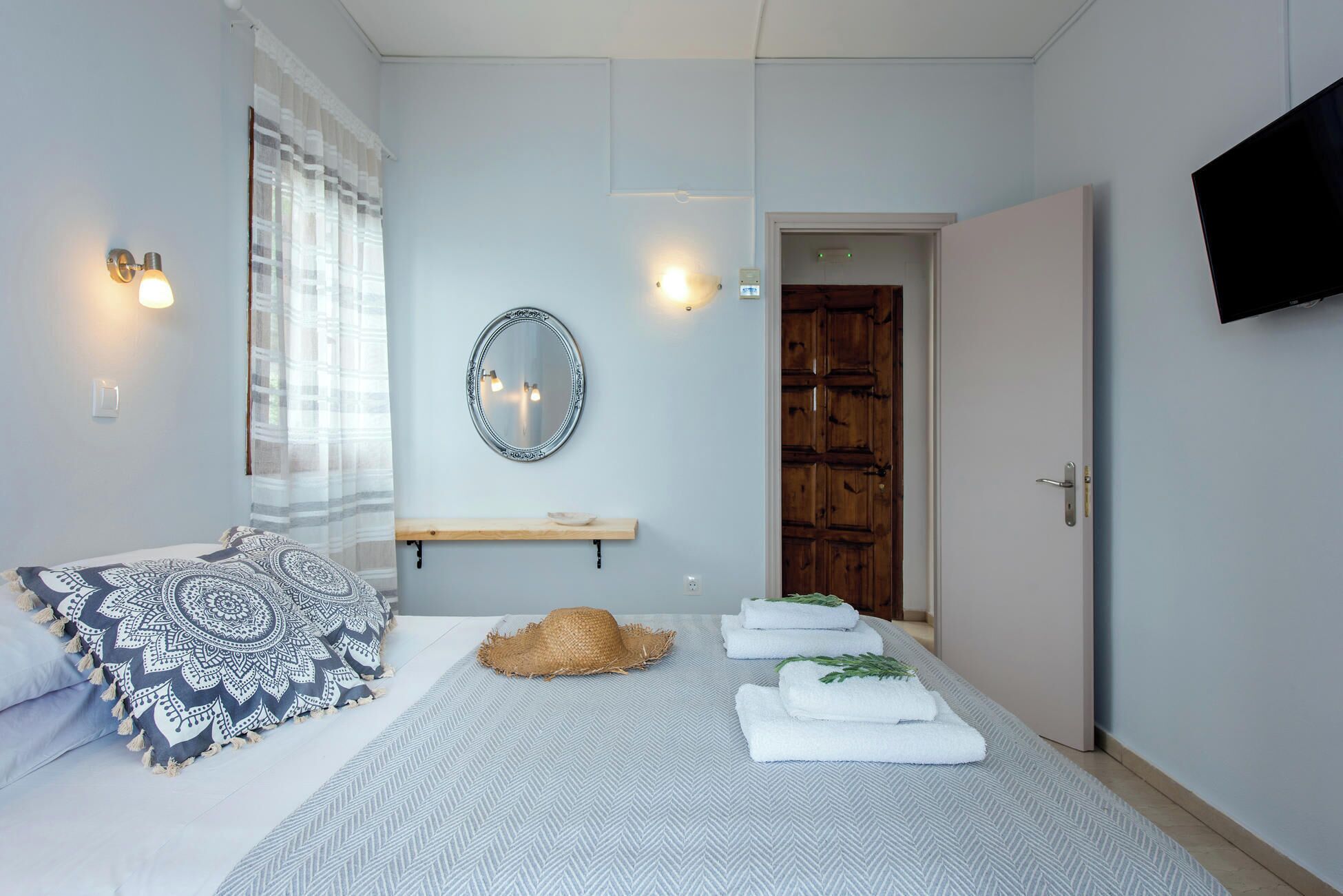 Une chambre à coucher comprenant un lit, une table de chevet, un miroir, une porte en bois et un téléviseur fixé au mur.