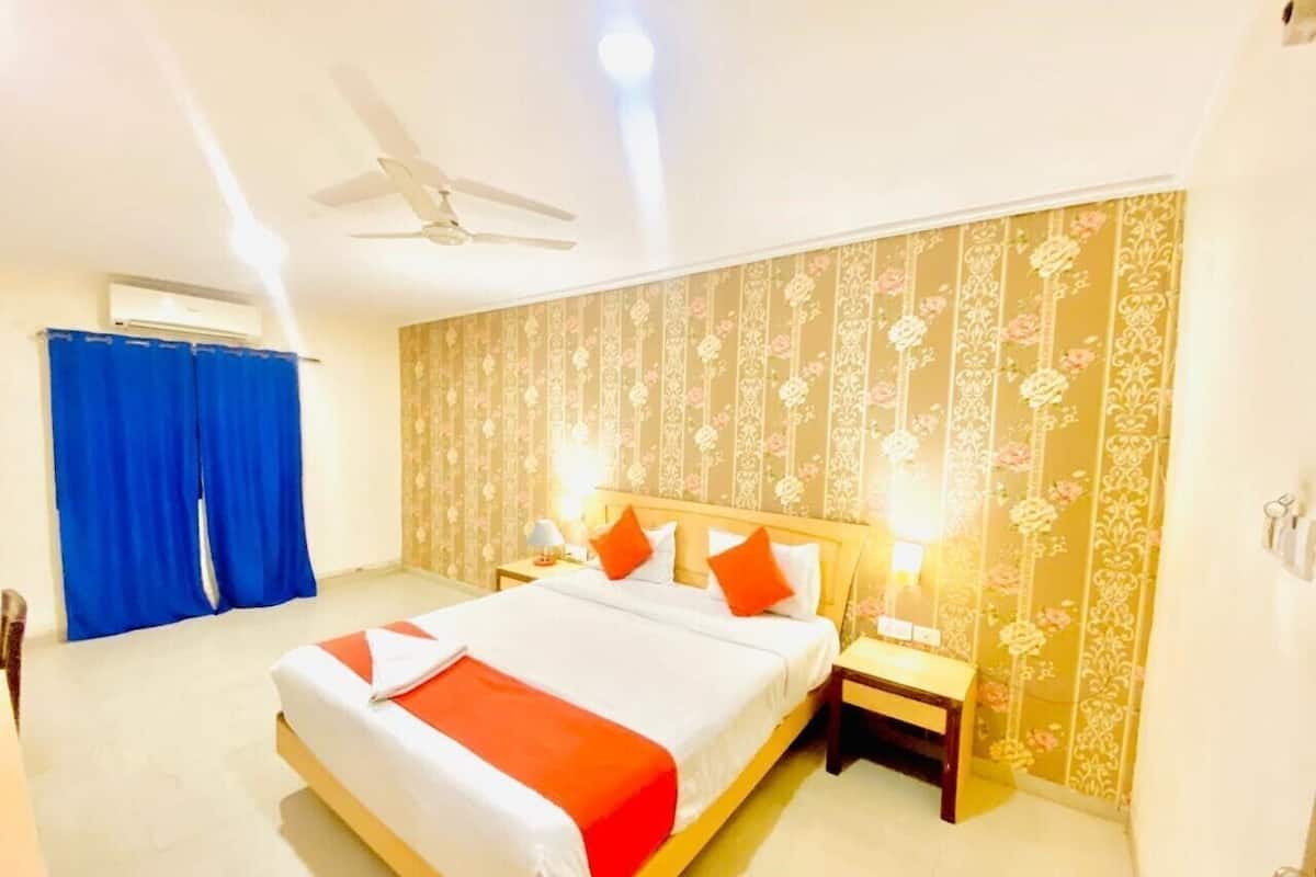 A hotel room with a large bed, two bedside tables, a ceiling fan, and floral wallpaper.